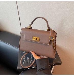 Detail of brown litchi pattern leather Kelly bag with golden twist lock and chain charm