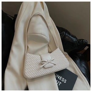 Detail of white woven underarm bag with decorative leather bow on a blazer