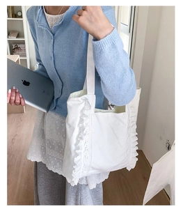 Detail of white canvas tote bag featuring delicate ruffle edges and spacious design