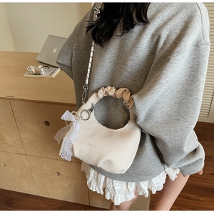 Detail of beige half-moon crossbody bag featuring lace pearl bow and silver chain strap