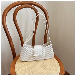 Close-up of a cream woven baguette bag with a bow knot detail on a vintage chair