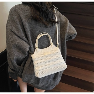 Detail of white woven bucket bag with leather strap worn by model on dark stairs