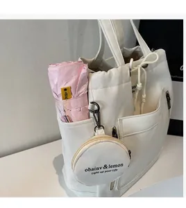Detail of white canvas tote bag showing side pocket holding a pink folding umbrella