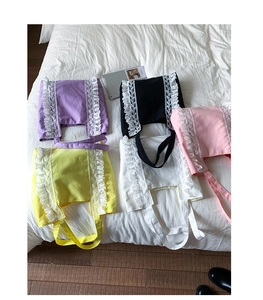 Flat lay of colorful canvas tote bags with white lace edges on a white bedsheet