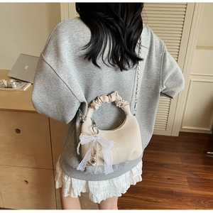 Detail of crescent shoulder bag featuring lace bow, pearl charm and metal chain strap