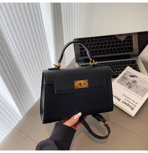 Detail of black crossgrain leather Kelly bag with gold twist lock on office desk