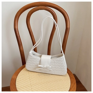 Close-up of white woven shoulder bag with leather bow detail on a rustic wooden chair