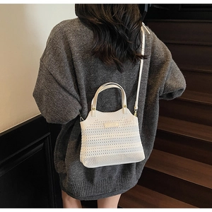 Detail of white hollowed-out woven tote bag with gold hardware and logo on wooden steps