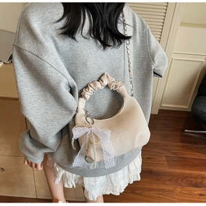 Detail of a beige crescent bag featuring lace bow, pearl charms and silver chain strap