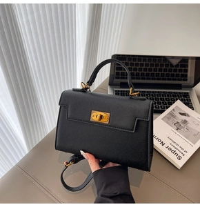 Detail of black pebbled leather handbag with gold twist lock on office desk