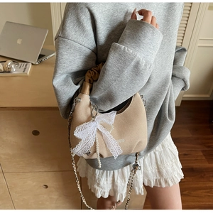 Detail of beige knit dumpling bag with silver chain, pearl charm, and lace bow accent
