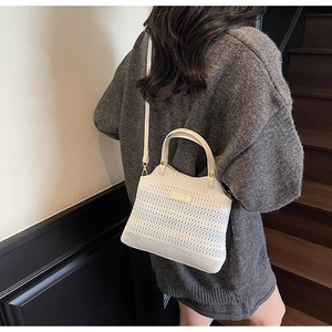 Detail of white hollow-out knit bucket bag showing golden studs and metal logo plate