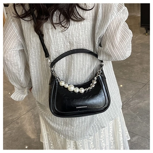 Détail du sac sous le bras en cuir noir brillant avec chaîne en perles et charme de cœur