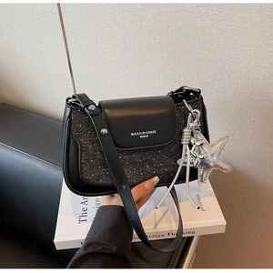 Close-up of black leather handbag with silver starfish charm and glitter texture on white book