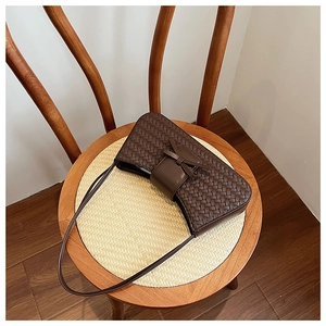 Detail of woven leather shoulder bag with a bow tie on a wooden chair seat