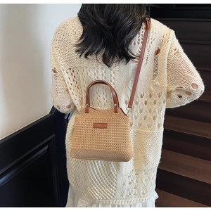 Close-up of beige woven crossbody bag with brown leather strap and brand logo patch