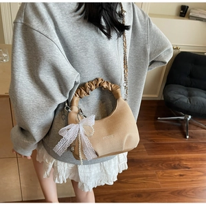 Close-up of beige chain bag featuring pleated handle and white lace bow with pearl charm
