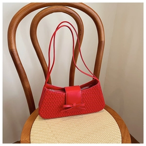 Detail of red woven underarm bag featuring an elegant leather bow and zip closure