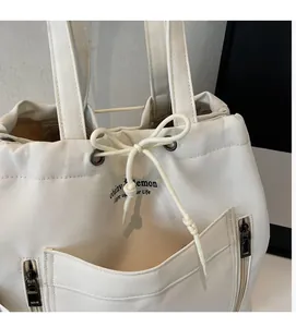 Close-up of white canvas tote bag with drawstring closure and black metal zipper pockets