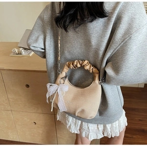 Detail of beige woven dumpling bag featuring pleated handle, chain strap and pearl bow charm