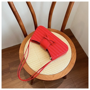 Top view of a red woven underarm bag with a bow detail on a woven chair pad