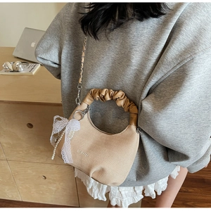 Detail of beige woven half-moon bag with bow pearl charm and silver chain strap