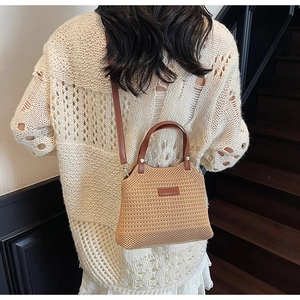 Detail of hand-woven knit bucket bag featuring brown leather straps on a beige sweater