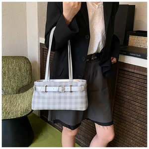 Detail view of a plaid baguette bag with buckle strap on a model shoulder