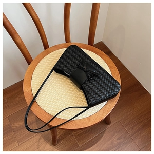 Detail of black woven underarm bag with decorative bow on a natural texture background