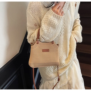 Detail of woven straw bucket bag featuring brown leather strap and brand logo patch
