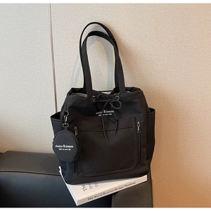 Detail of black canvas tote bag showing side pocket, drawstring closure and round pouch