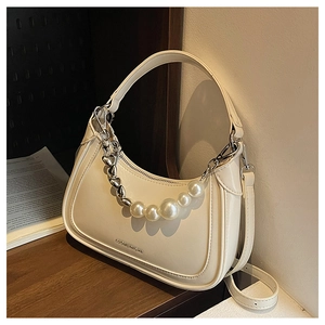 Detail der cremefarbenen Hobo-Tasche mit Perlenherzkette und verstellbarem Gurt auf Holz