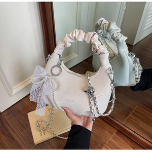 Close-up of cream woven dumpling bag with pearl lace bow and gold chain strap
