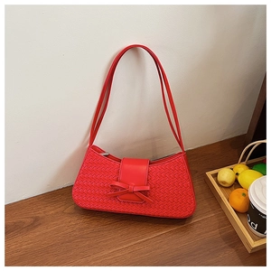 Detailed close-up of a red woven baguette bag with bow detail on a rustic wooden desk
