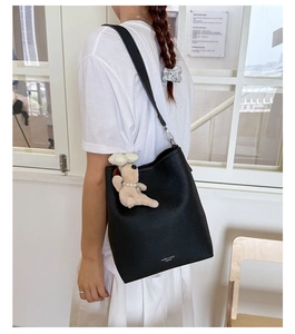 Detail of black bucket bag with lychee texture and cute plush puppy charm accessory