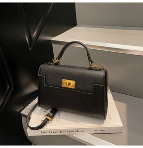 Detail of black Saffiano leather handbag with gold twist lock and chain strap on books