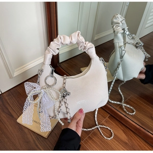 Detail of cream hobo bag with cloud-shaped handle and pearl lace bow charms