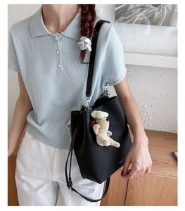 Detail of black pebbled leather bucket bag with cute plush dog charm on a model