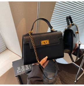 Detail of black textured leather handbag with gold twist lock and elegant chain strap