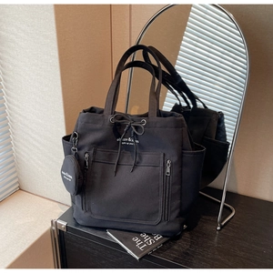 Detailed shot of a black canvas tote bag featuring double front zipper pockets and drawstring