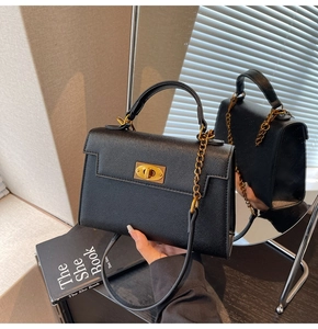 Detail of black lychee-grain handbag featuring golden turn-lock and chain strap on a mirror