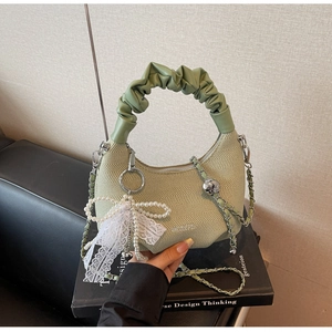 Detailed close-up of light green woven handbag with pearl bow charm and silver chain