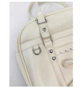 Close-up of cream PU leather bag featuring heart rivets, D-rings and wavy stitching detail