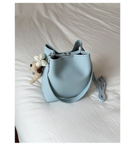 Detail of light blue leather bucket bag with plush charm on white bedding