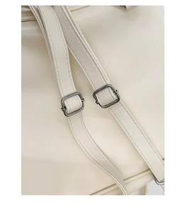 Detailed close-up of silver metal buckles and stitching on creamy white PU leather strap