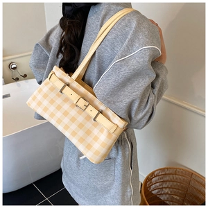 Detail view of yellow checkered hobo bag with belt buckle on shoulder of model