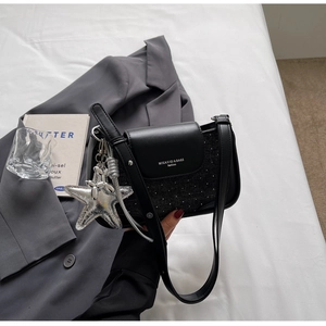 Detail of black crossbody bag with matte faux leather and silver star charm accessory