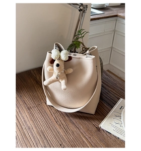 Detail of cream bucket bag with litchi texture and cute plush puppy keychain