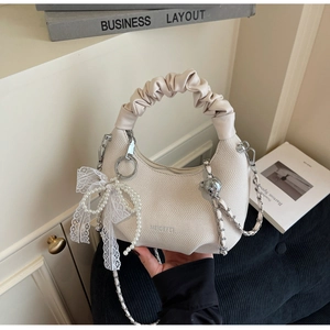 Detail of beige crossbody bag with pearl charms, lace bow, and chain strap detail