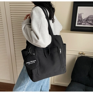 Detail of black canvas tote bag showing side zipper pocket and round pouch on model